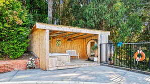 A wooden outdoor hot tub area with a bench and a statue, surrounded by a pool and a fence. - Serene Canyon Private Villa•Pool•HotTub•Sauna Retreat STR Permit Number:14614552 (Pacifica)