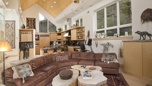 A spacious living area with a large brown leather sectional sofa, a coffee table, and a kitchen in the background. - Sandstone Chalet (Vail)