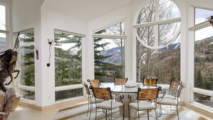 A dining area with a round table and six chairs, large windows with mountain views, and a decorative horse sculpture. - Sandstone Chalet (Vail)