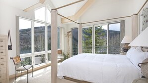 A bedroom with a large bed, a chair, a dresser, and a window with a mountain view. - Sandstone Chalet (Vail)