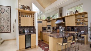 A spacious kitchen with wooden cabinets, a central island with bar stools, and a large window providing natural light. - Sandstone Chalet (Vail)