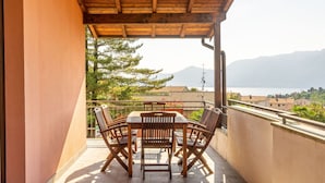A wooden pergola-covered balcony with a table and chairs, overlooking a body of water and mountains. - Cosy apartment for 6 guests with A/C, WIFI, pool, TV and terrace (Luino)
