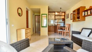 A living room with wicker furniture, a dining area with wooden chairs, and a kitchen visible through an open door.