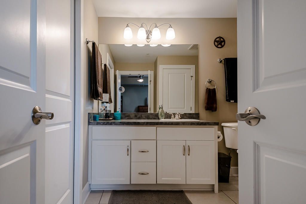 A bathroom with white cabinets, a sink, and a mirror. There is a towel rack above the mirror and a towel hanging on it.