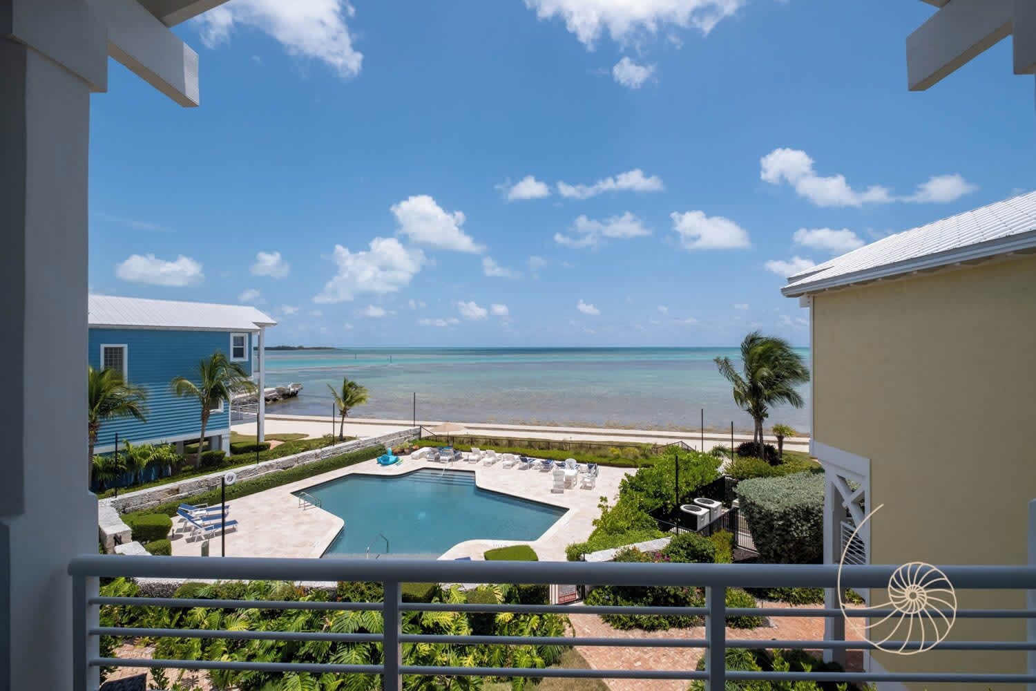 A pool with lounge chairs, a view of the beach, and a clear sky.