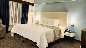 A hotel room with a large bed, a nightstand with a phone, a lamp, and a chair.