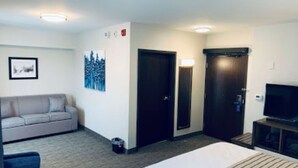 A hotel room with a bed, a sofa, a TV, and two doors.