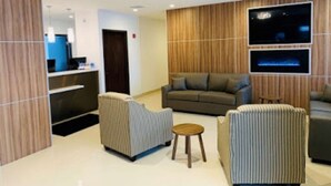 A modern lobby with a reception desk, sofas, and a TV screen.