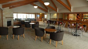 Un vaste espace intérieur agrémenté de poutres en bois, de nombreux coins salon avec des tables et des chaises rondes, une cheminée et un bar doté d’un comptoir et d’étagères.