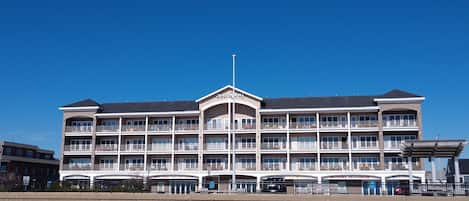 Um hotel de vários andares com um átrio central, varandas e céu claro.