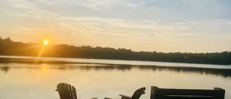 Une jetée avec deux chaises Adirondack donnant sur un lac paisible au coucher du soleil.