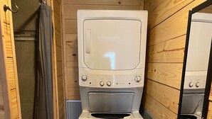 A compact bathroom with a washing machine, a shower, and a mirror.