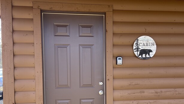 A wooden cabin with a brown door, a welcome sign, and a mailbox.