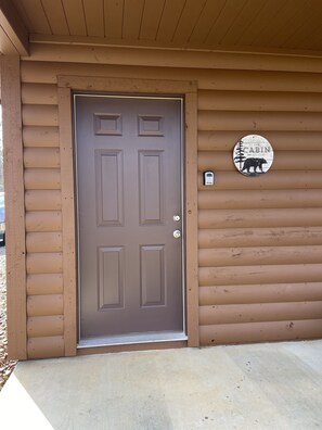 A brown wooden cabin door with a metal handle and a welcome sign on the wall.