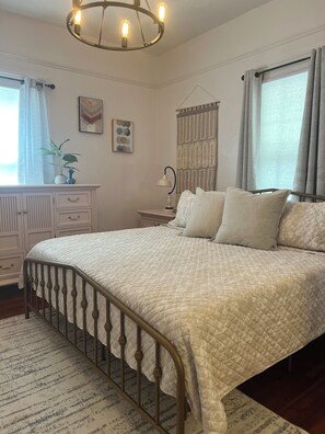 A bedroom with a bed, bedside table, lamp, curtains, and a wall-mounted light fixture.