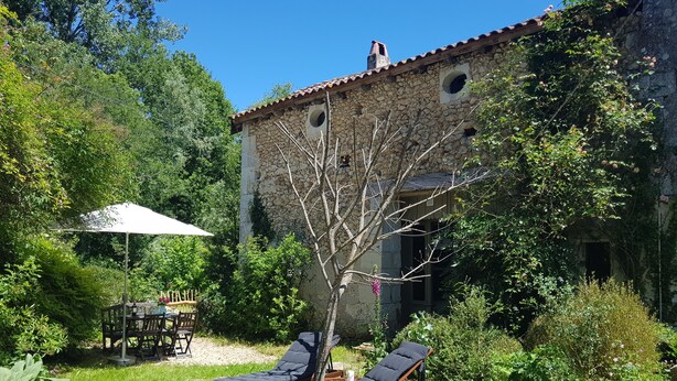 A stone building with a tiled roof, a circular window, and a tree in the foreground.