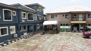 A building with multiple floors, air conditioning units, a covered entrance, and a paved courtyard. - Stunning 3-Bed House in well Secured Estate, Lekki (Awoyaya, Ibeju Lekki LG.)