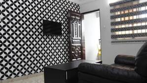 A room with a patterned wall, a black cabinet, a leather sofa, and a door with decorative elements. - Stunning 3-Bed House in well Secured Estate, Lekki (Awoyaya, Ibeju Lekki LG.)
