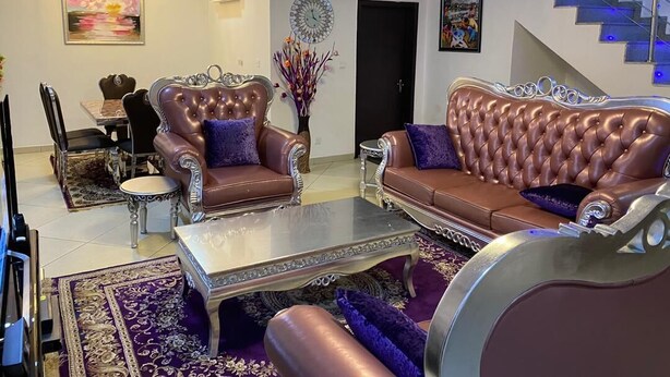 A living room with a sofa, armchairs, and a coffee table. There is a staircase with blue lighting and a door in the background. - Furnished 4 Beds Semi-Det House in Abuja, Nigeria (Abuja)
