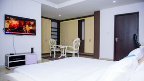 A hotel room with a large bed, a TV mounted on the wall, a desk with two chairs, and a wardrobe. - Furnished 4 Beds Semi-Det House in Abuja, Nigeria (Abuja)