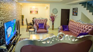 A living room with a television, a sofa, a chair, and a decorative wall. - Furnished 4 Beds Semi-Det House in Abuja, Nigeria (Abuja)