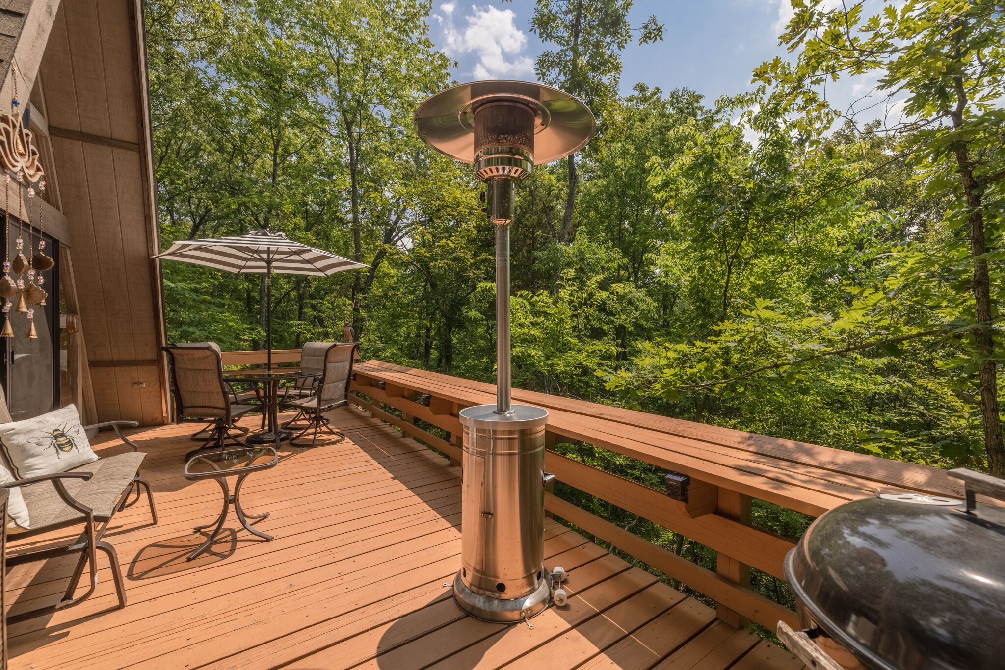 Una terraza de madera con mobiliario exterior, una parrilla y un calentador portátil.