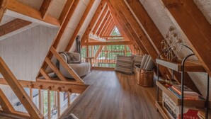 Een slaapkamer op zolder met houten balken, een houten vloer, een bank, een bijzettafeltje en een boekenplank.