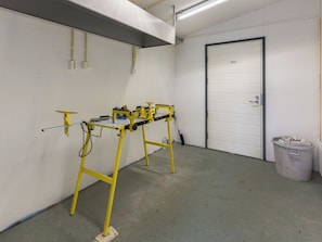 A room with a yellow workbench, a door, and a trash bin.