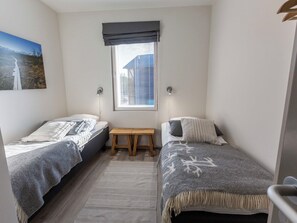 Una habitación pequeña y luminosa con dos camas individuales, un banco y una ventana con persianas.