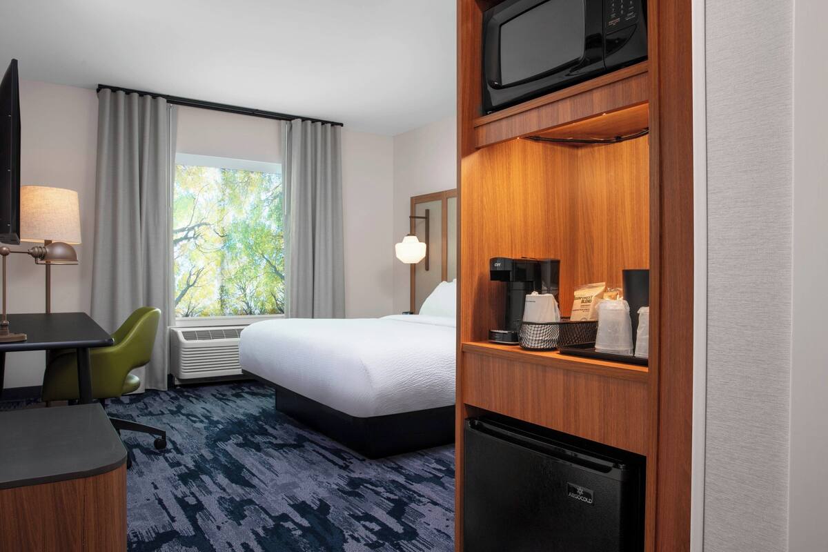 Ein Hotelzimmer mit einem Bett, einem Schreibtisch, einem Sessel, einer Mikrowelle, einer Kaffeemaschine und einem Kühlschrank.