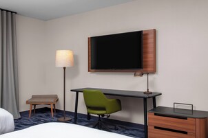 Habitación de hotel con una cama, un escritorio con una silla, un televisor, una lámpara y una mesita.
