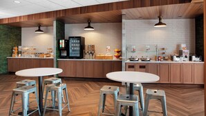 A modern kitchen area with wooden cabinets, white brick walls, and stainless steel appliances. There are two round tables with stools, a refrigerator, and a coffee machine. - Fairfield Inn & Suites by Marriott Lebanon near Expo Center (Lebanon)