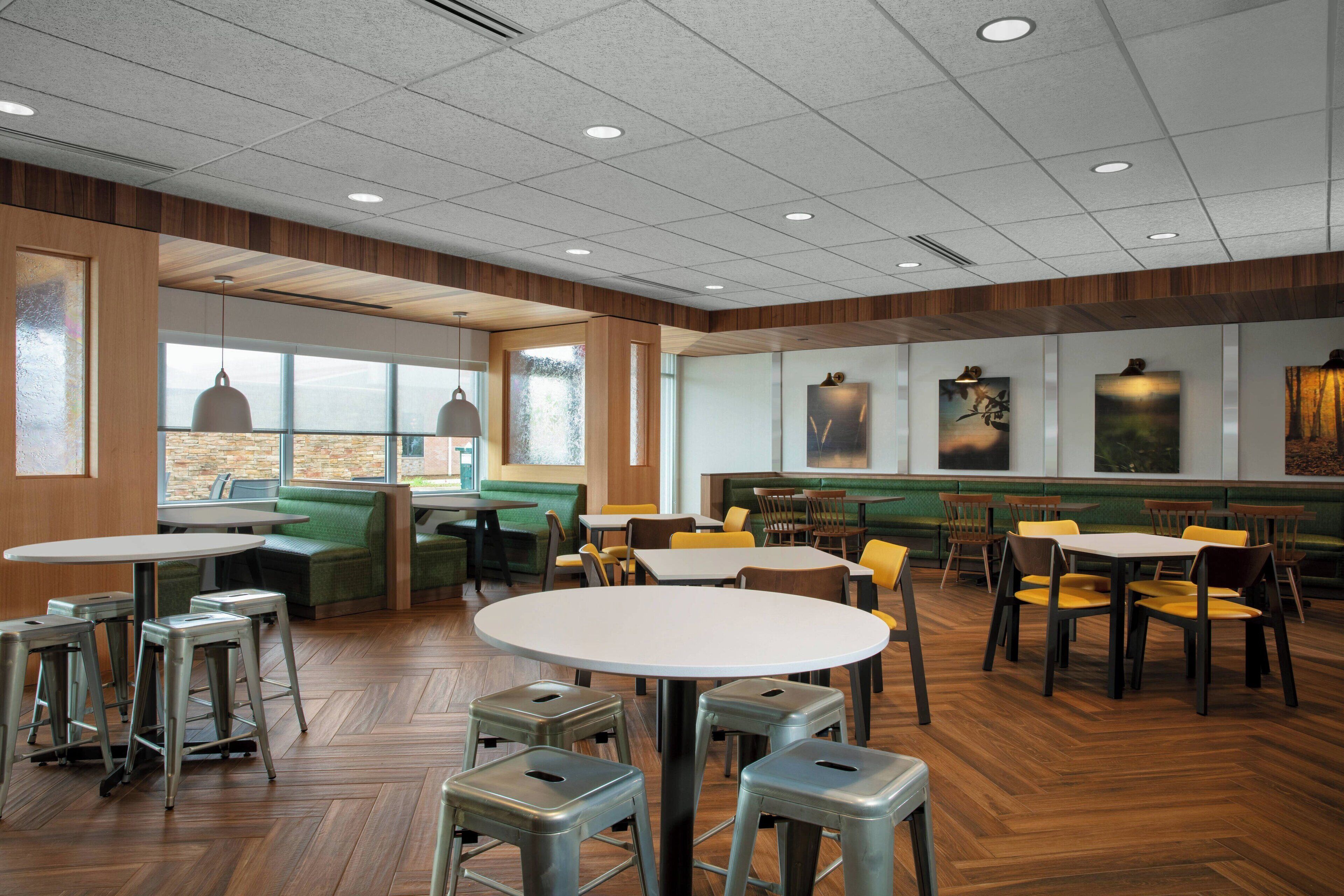 Restaurante com piso de madeira, cabines verdes, cadeiras amarelas e mesas brancas.