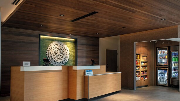 A reception desk with a modern design, a large decorative wall piece, and a refrigerator stocked with beverages. - Fairfield Inn & Suites by Marriott Lebanon near Expo Center (Lebanon)