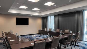 Un salón de conferencias con una larga mesa, sillas, botellas de agua y un televisor de pantalla plana en la pared.