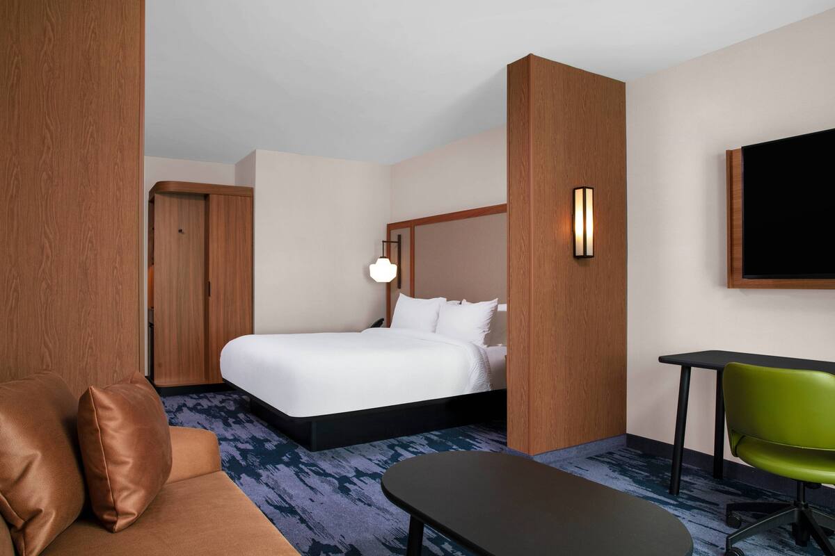 Ein Hotelzimmer mit einem Bett, einem grünen Sessel, einem Schreibtisch und einem an der Wand befestigten Fernseher.