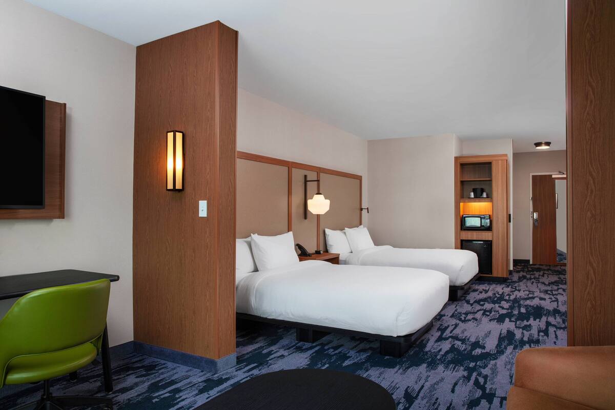 Ein Hotelzimmer mit zwei Betten, einem Schreibtisch, einem Sessel, einem Fernseher und einer Lampe.