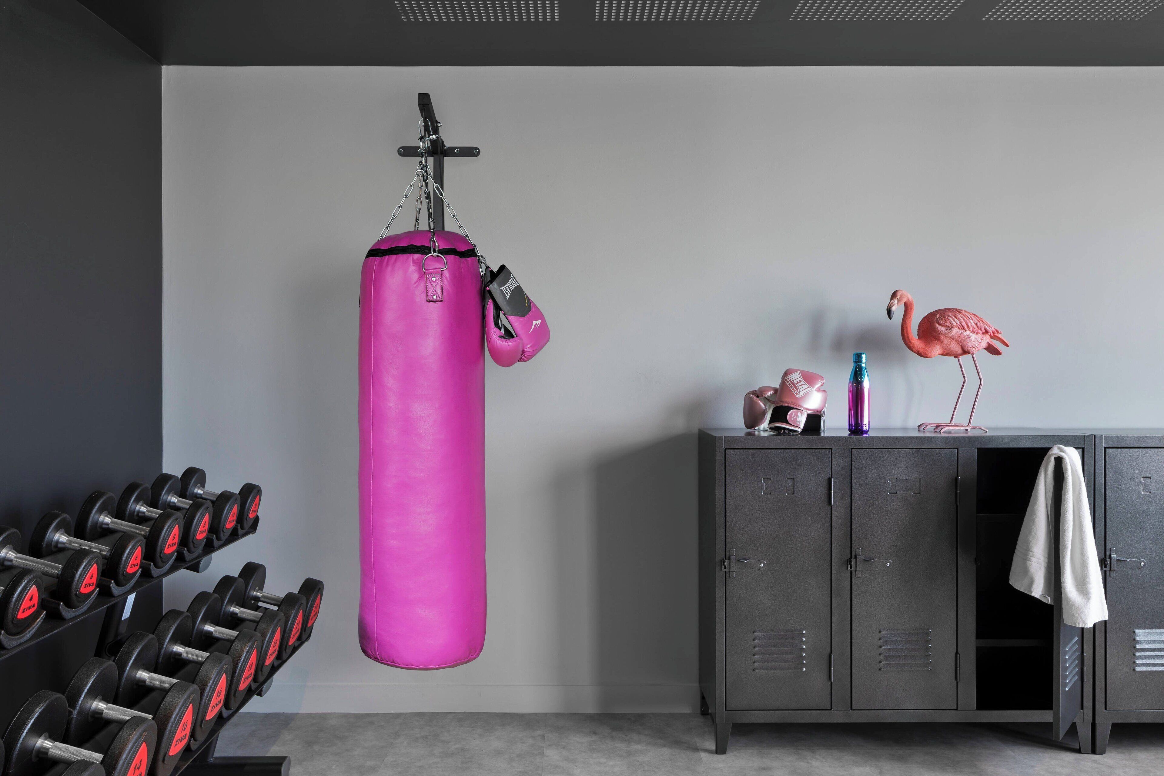 Un gimnasio con un saco de boxeo rosa, mancuernas y un armario decorado con un flamenco.