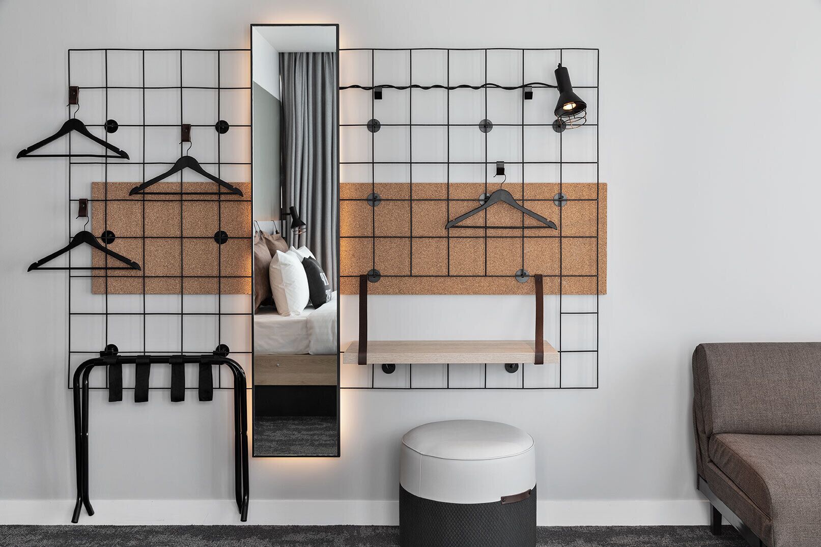 A room with a corkboard wall, a mirror, a hanging rack, a small round table, and a bench.