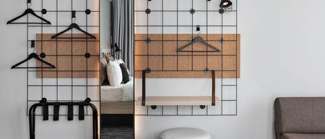 A room with a corkboard wall, a mirror, a hanging rack, a small round table, and a bench.