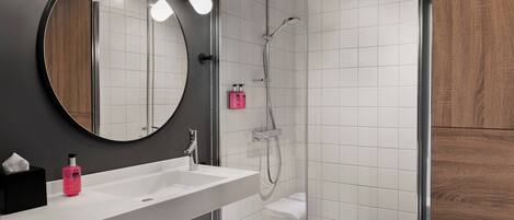 A modern bathroom with a large mirror, a white sink, and a glass-enclosed shower area.