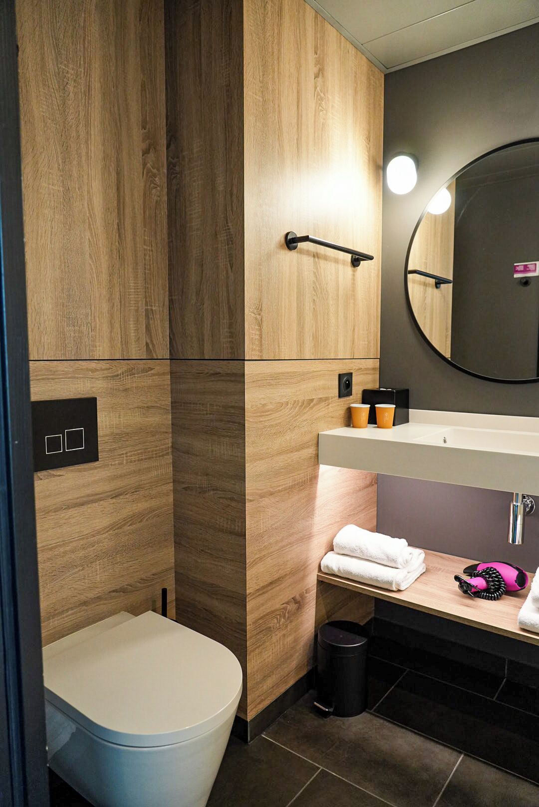 A modern bathroom with a toilet, vanity, mirror, and towel rack.