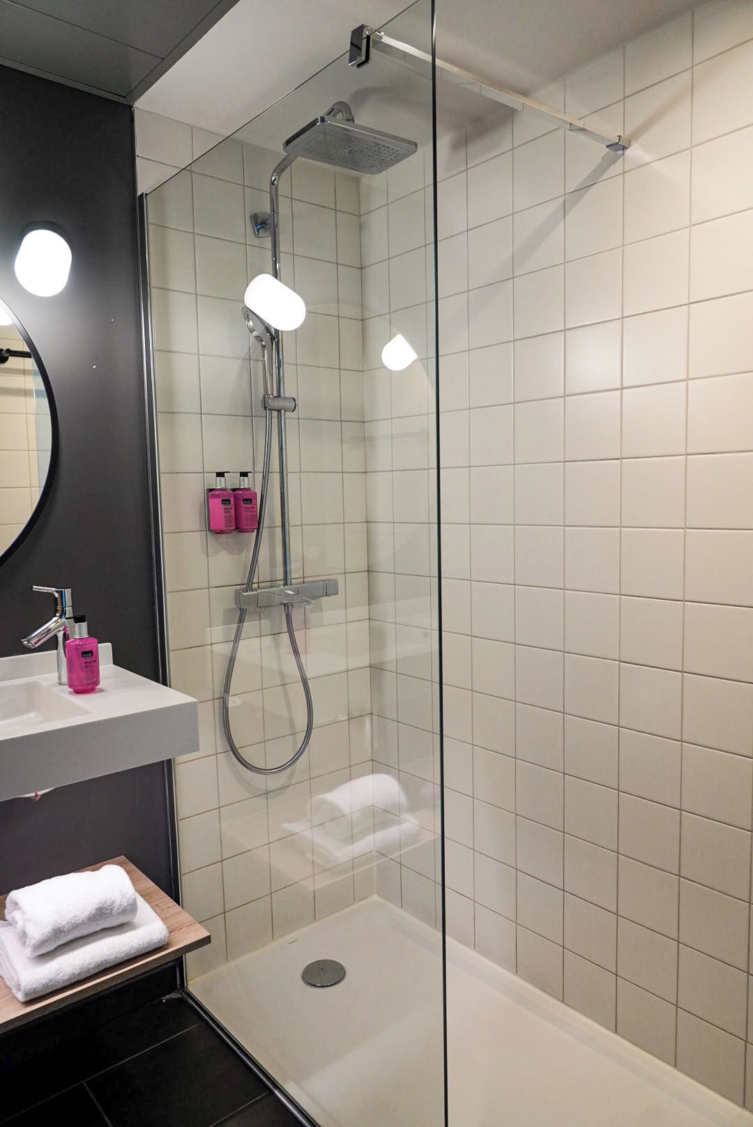 Un baño moderno con ducha de vidrio, un lavamanos blanco con espejo y un perchero para toallas.