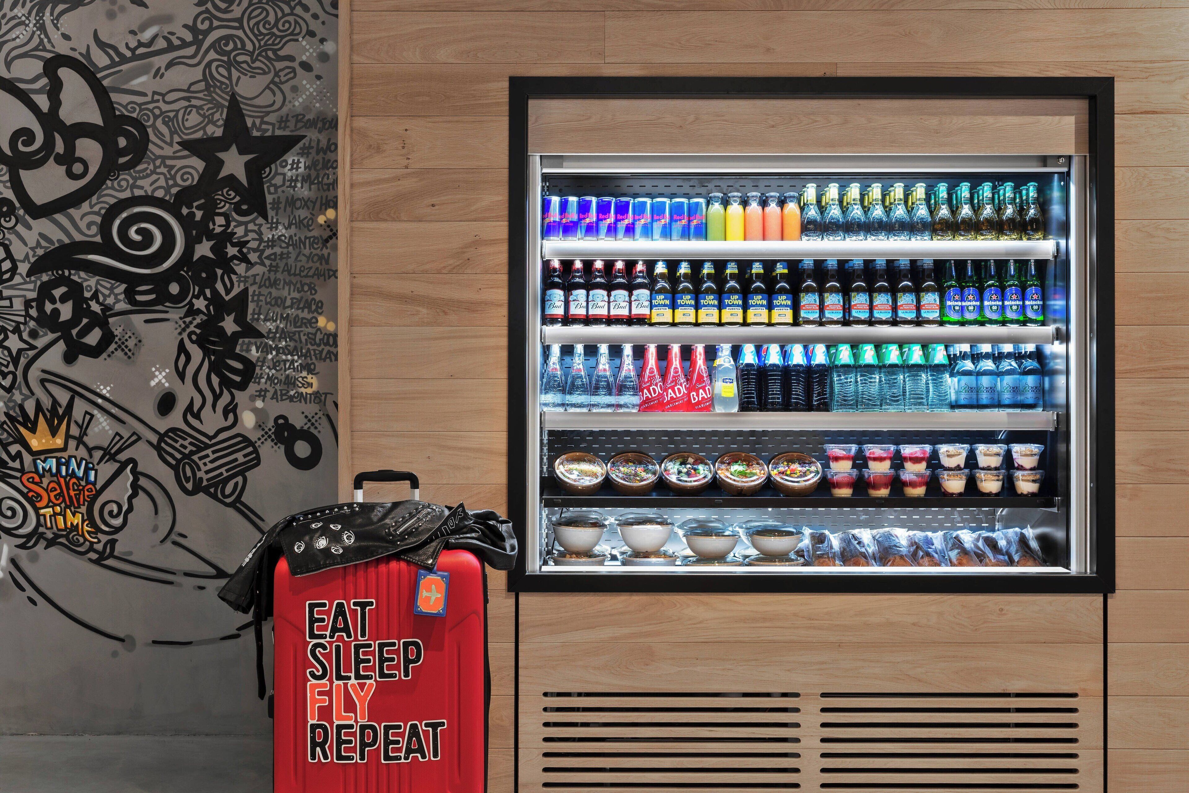 Ein Getränkeautomat mit verschiedenen Getränken und Snacks, ein roter Koffer mit motivierendem Spruch und eine Wand mit Wandmalerei im Graffiti-Stil.