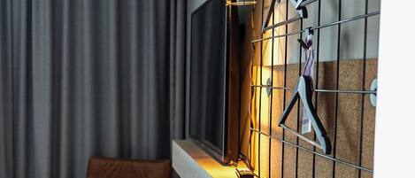 Une chambre d’hôtel moderne, dotée d’un bureau en bois, d’une chaise, d’un portant métallique pour les vêtements et d’une fenêtre avec des rideaux.