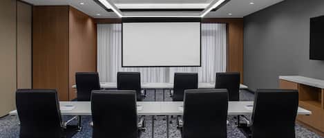 A conference room with a large screen, black chairs, and a carpeted floor.