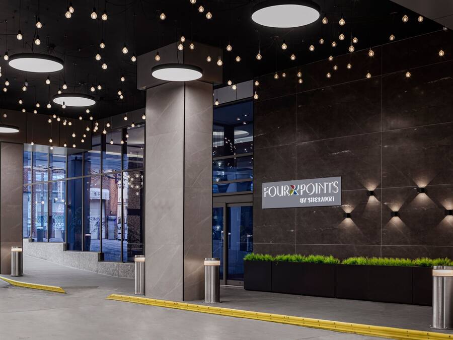 Recepció d'hotel moderna amb un gran rètol que diu "Four Points by Sheraton", amb interior fosc, múltiples llums penjants i entrada de vidre.