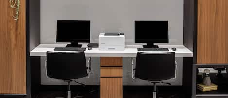 A modern office desk with two monitors, a printer, and two black office chairs.
