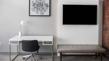 A modern room with a white desk, black office chair, a framed abstract artwork, a large flat-screen TV, and a bench.
