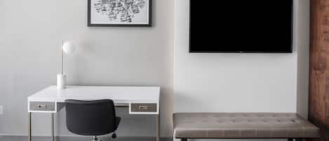 A modern room with a white desk, black office chair, a framed abstract artwork, a large flat-screen TV, and a bench.